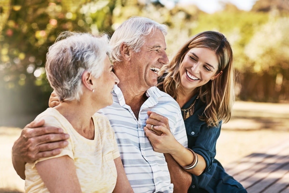 A smiling group of three people sitting outdoors, including an elderly couple and a younger woman.