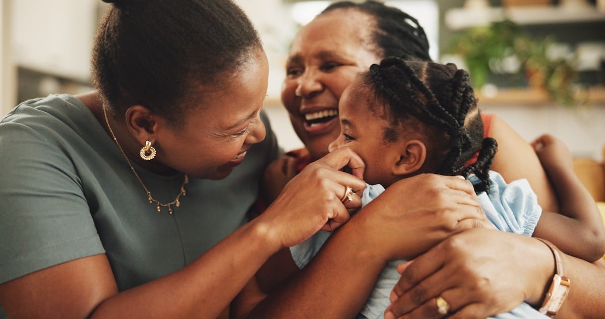 Three people joyfully interacting, with two women and a child laughing together, showcasing warmth and affection.